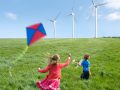 Children playing with kite and glider in front wind turbines.
